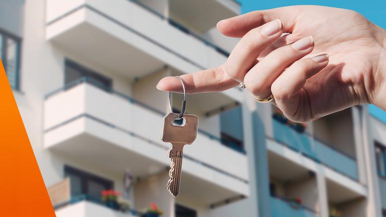 Wohnungsschlüssel in der Hand vor einem Mehrfamilienhaus