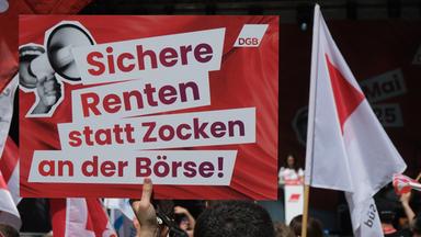 Ein Transparent mit dem Aufdruck "Sichere Renten statt Zocken an der Börse!" und Fahnen werden bei einer Veranstaltung des DGB zum ersten Mai in die Höhe gehalten. 