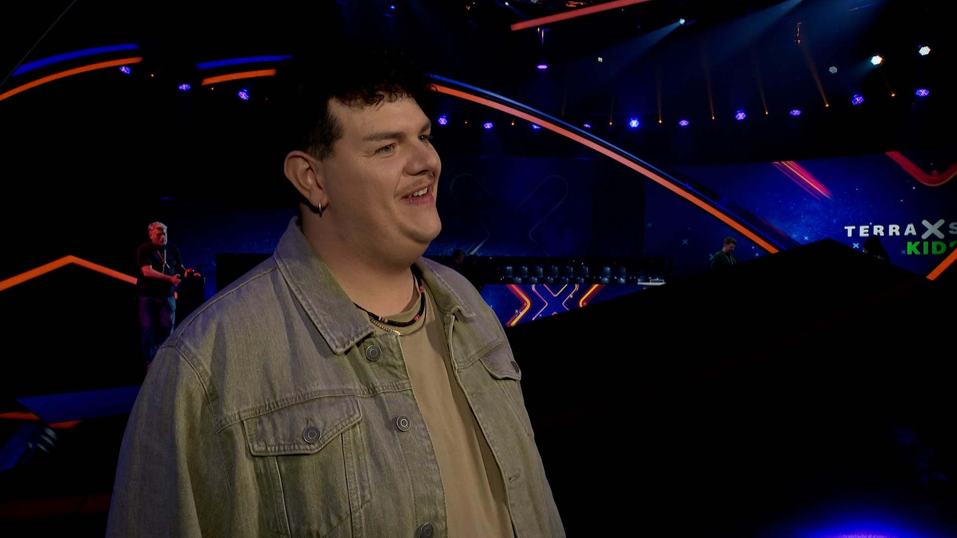 Isaak lächelt an der kamera vorbei. Im Hintergrund die Kulissen von Terra X Kids