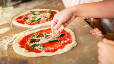 Man sieht eine Pizza, die gerade zubereitet wird. 