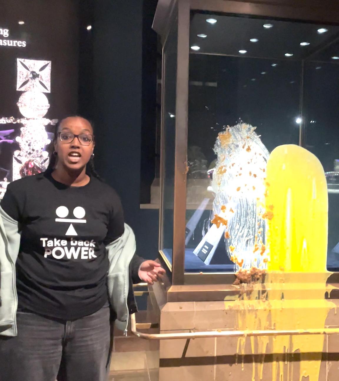 Essensanschlag auf die Kronjuwelen: zwei Aktivisten stehen vor den Kronjuewlen im Tower of London, auf die sie Apfelkuchen mit Vanillesoße gekippt haben