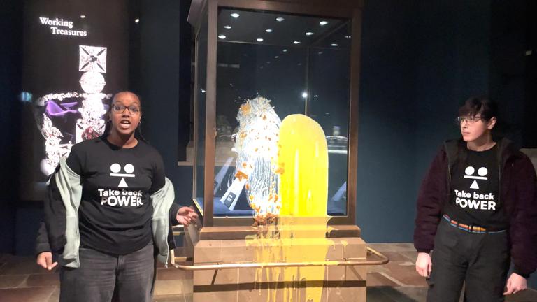 Essensanschlag auf die Kronjuwelen: zwei Aktivisten stehen vor den Kronjuewlen im Tower of London, auf die sie Apfelkuchen mit Vanillesoße gekippt haben