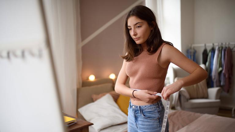 Junges Teenager-Mädchen schaut in ihrem Zimmer in den Spiegel.
