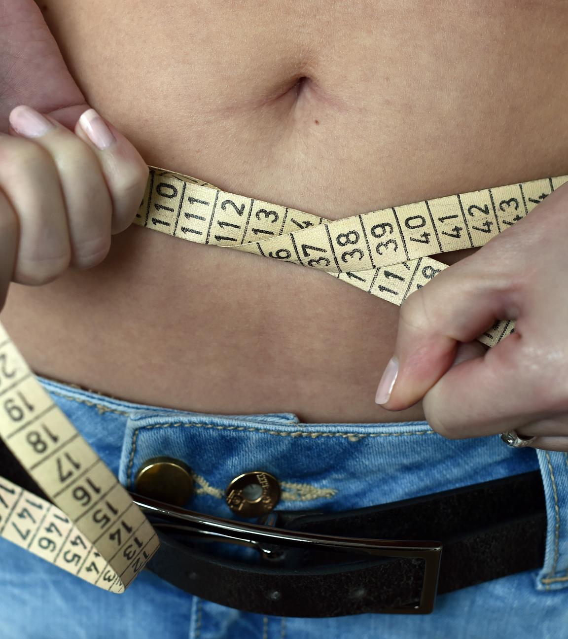 Eine junge Frau legt ein Maßband um ihren Bauch.