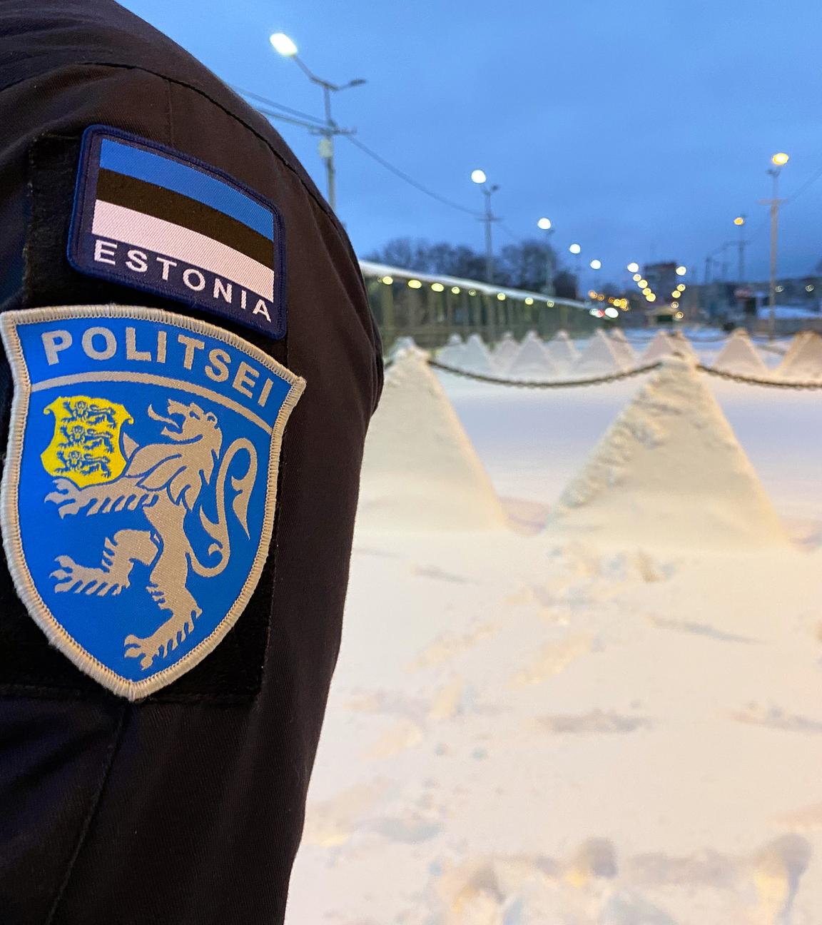 Arm eines Polizisten, im Hintergrund die estnische Grenze zu Russland