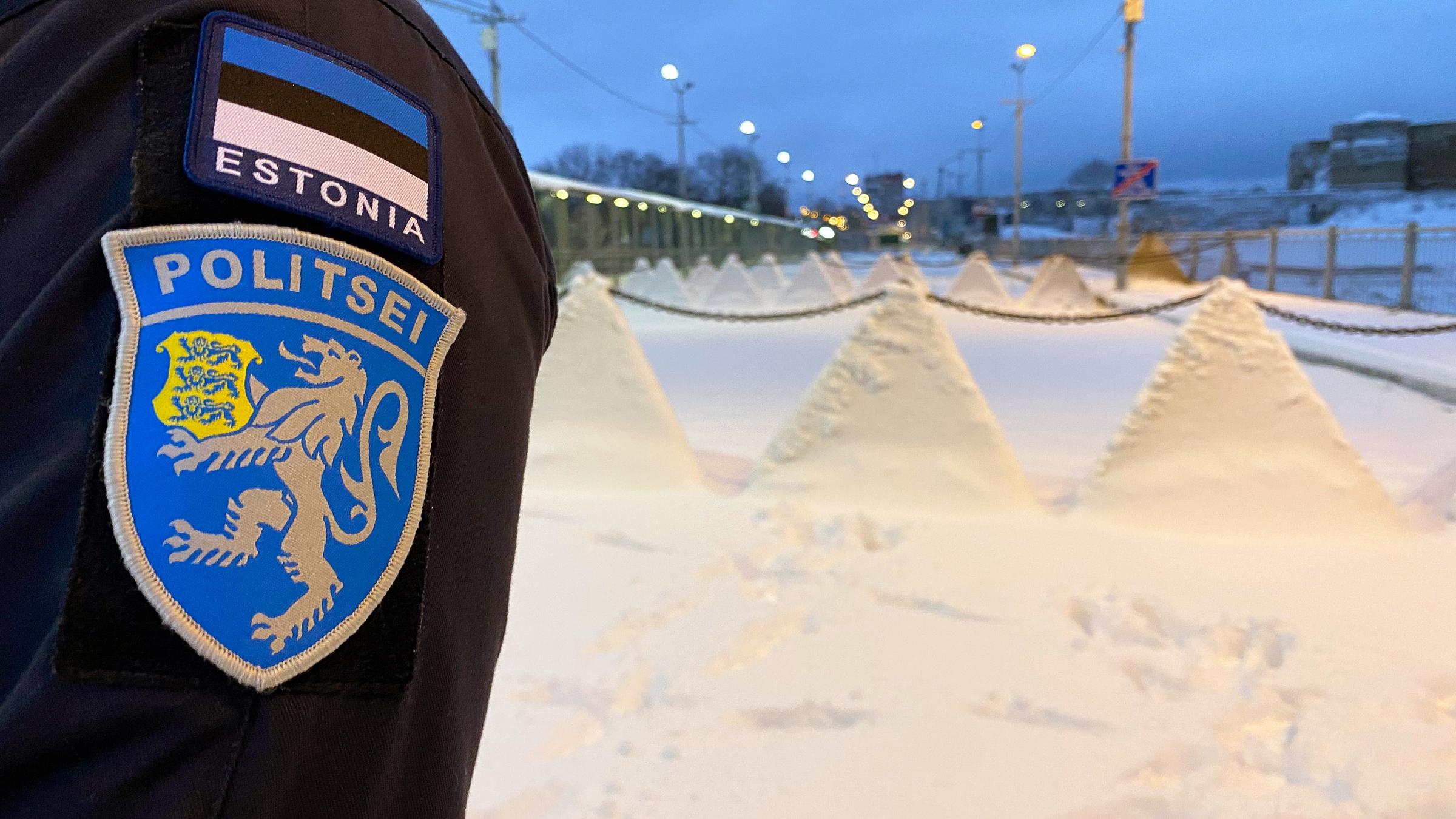 Arm eines Polizisten, im Hintergrund die estnische Grenze zu Russland