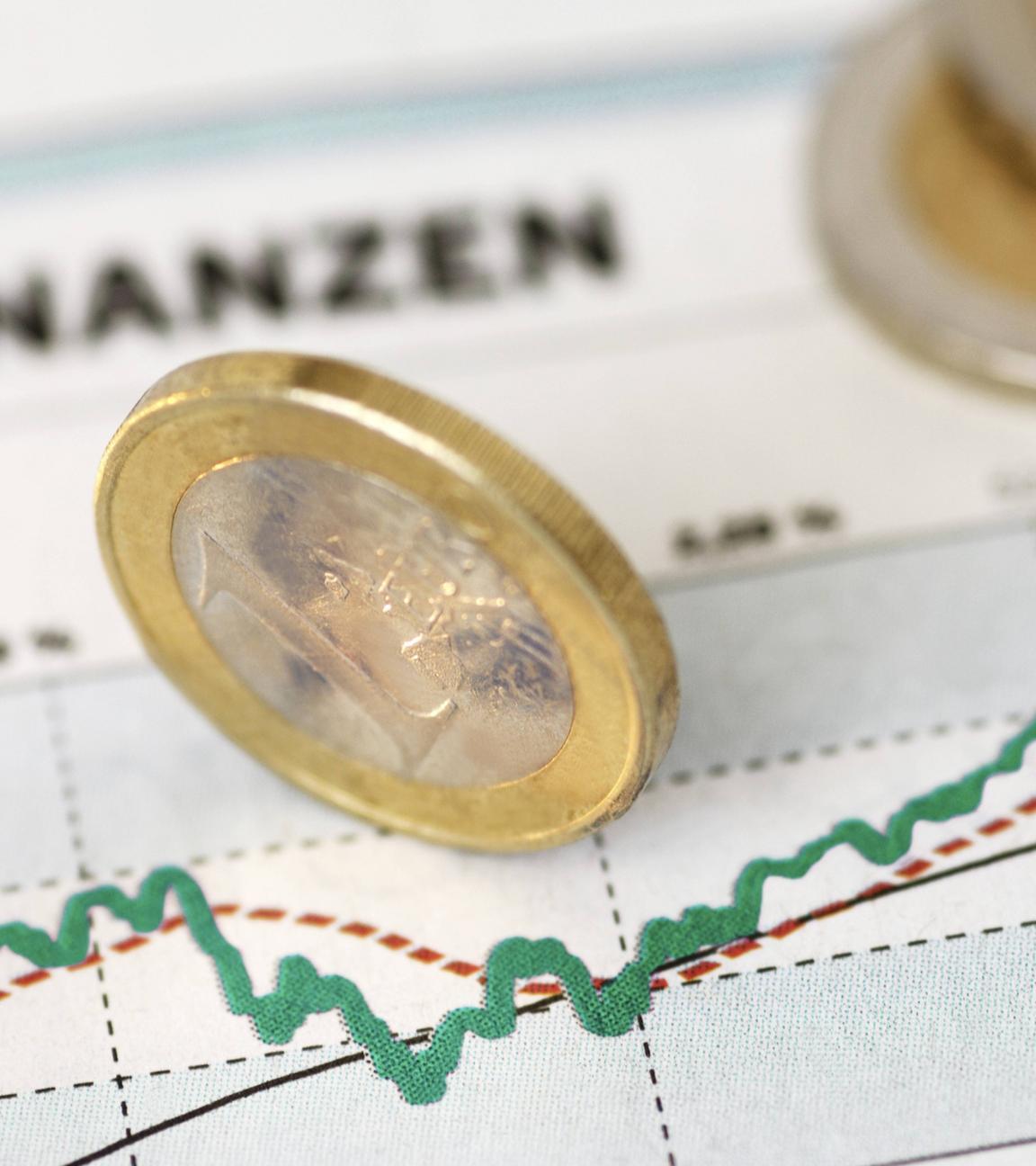 Ein-Euro-Stück aufgestellt auf Ausdruck einer Grafik mit Finanzkurve