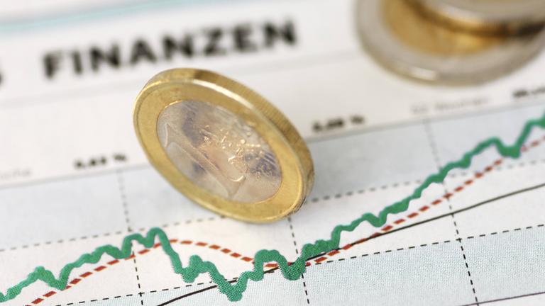 Ein-Euro-Stück aufgestellt auf Ausdruck einer Grafik mit Finanzkurve