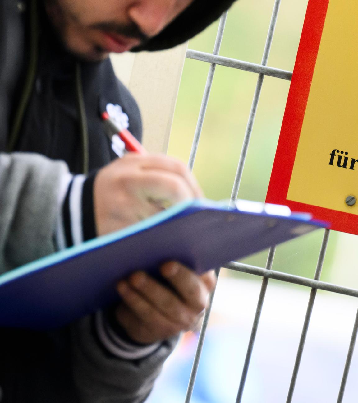 Ein Mann füllt ein Formular aus neben einem Schild vom Bundesamt für Migration und Flüchtlinge an der Landesaufnahmebehörde Niedersachsen