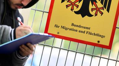 Ein Mann füllt ein Formular aus neben einem Schild vom Bundesamt für Migration und Flüchtlinge an der Landesaufnahmebehörde Niedersachsen