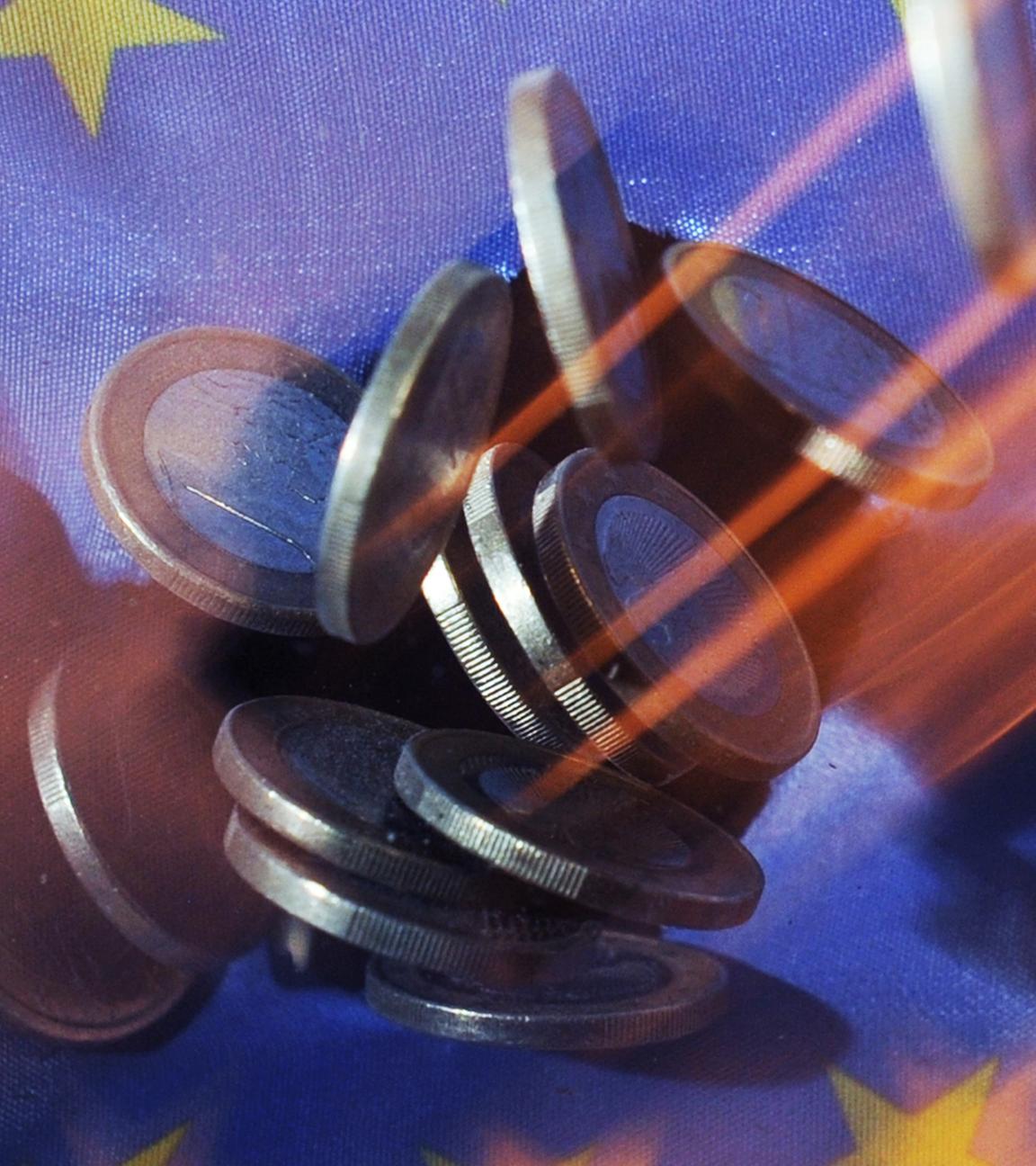 Auf eine Europaflagge fallen Euro-Münzen