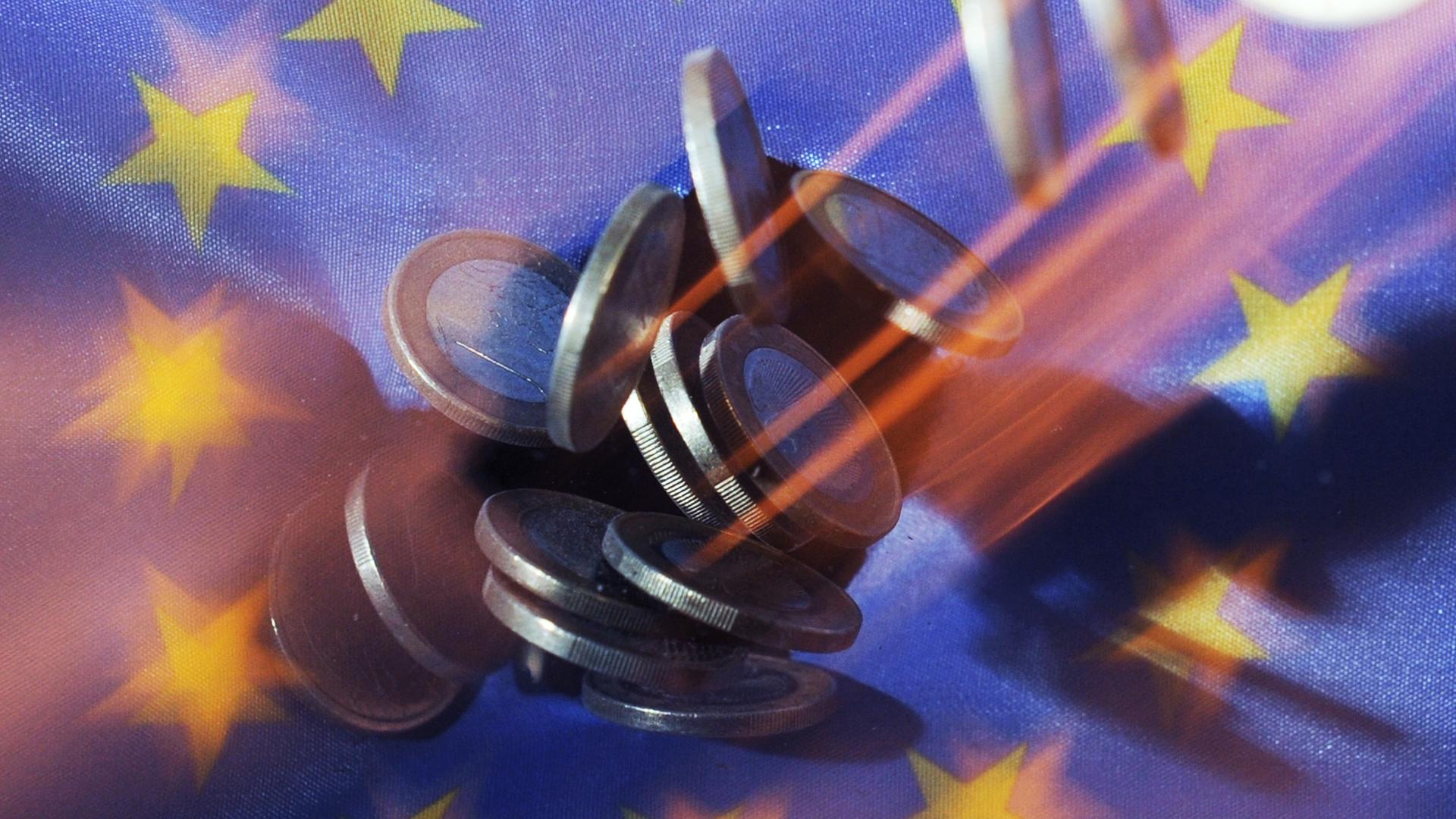 Auf eine Europaflagge fallen Euro-Münzen