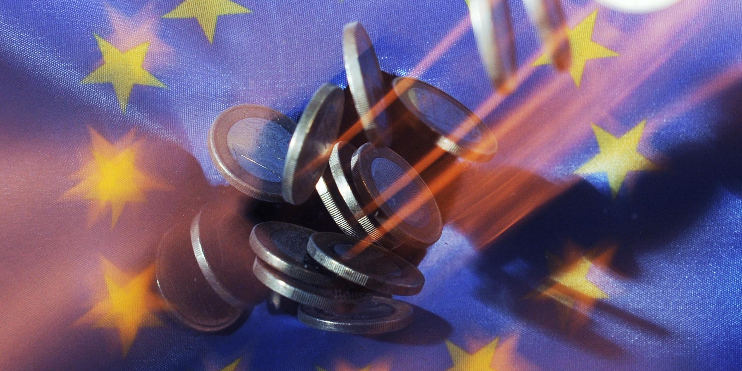 Auf eine Europaflagge fallen Euro-Münzen