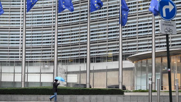 Belgien, Brüssel: EU-Flaggen wehen vor dem EU-Parlament in Brüssel. Unten hält ein Mensch einen Regenschirm.