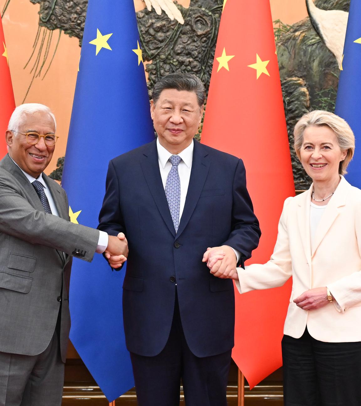 Links Antonio Costa, mittig Xi Jinping, rechts Ursula von der Leyen, hinter ihnen die Fahnen der EU und Chinas. Die drei lächeln und schütteln die Hände.
