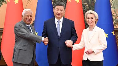 Links Antonio Costa, mittig Xi Jinping, rechts Ursula von der Leyen, hinter ihnen die Fahnen der EU und Chinas. Die drei lächeln und schütteln die Hände.