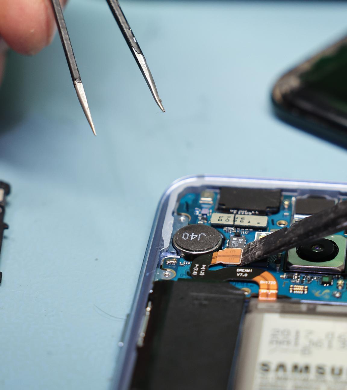  Ein Techniker arbeitet an einem Smartphone mit defektem Display in seinem kleinen Fachgeschäft für Reparaturen und Zubehör.