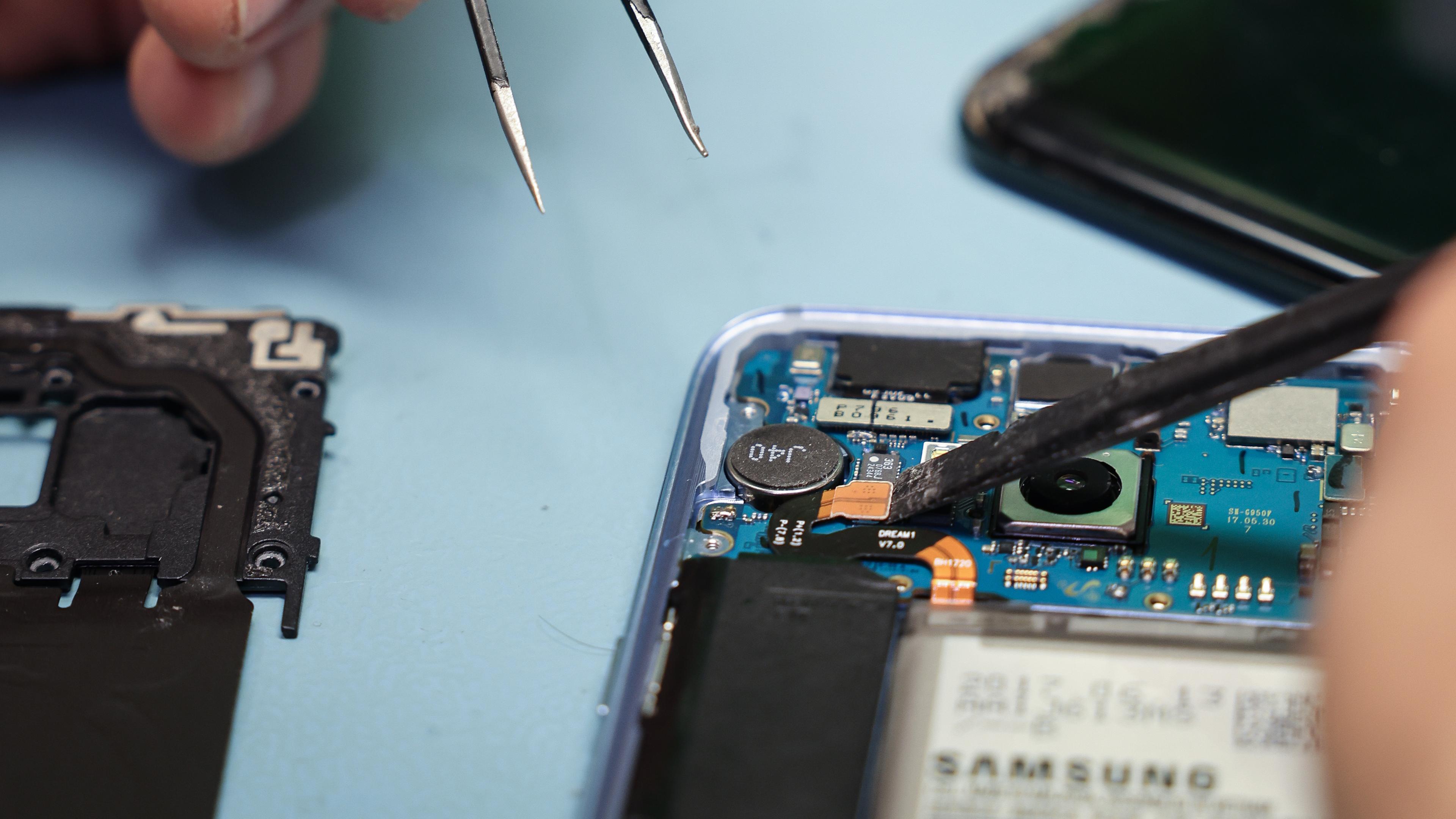  Ein Techniker arbeitet an einem Smartphone mit defektem Display in seinem kleinen Fachgeschäft für Reparaturen und Zubehör.