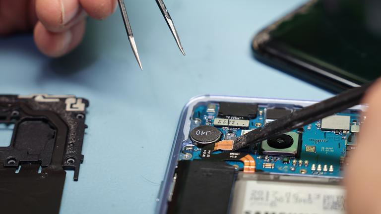  Ein Techniker arbeitet an einem Smartphone mit defektem Display in seinem kleinen Fachgeschäft für Reparaturen und Zubehör.