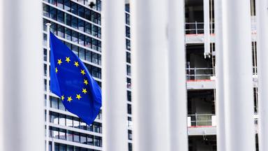 Eine Flagge der Europäischen Union (EU) weht vor dem Gebäude des Europäischen Parlaments und ist zwischen anderen Fahnenmasten hindurch zu sehen. 