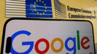 Eine Gesamtansicht zeigt ein Google-Logo auf einem iPhone-Bildschirm vor dem Gebäude der Europäischen Kommission in Brüssel.