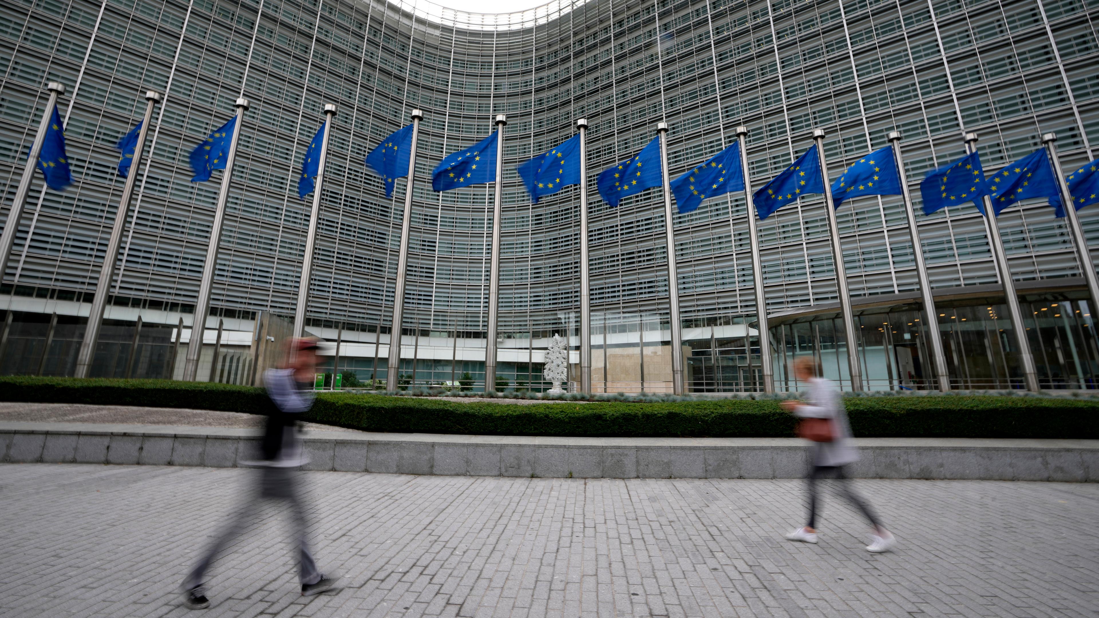 EU-Fahnen flattern im Wind, während Fußgänger am EU-Hauptsitz vorbeigehen. 