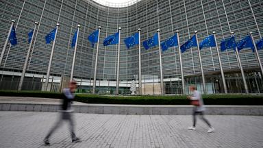 EU-Fahnen flattern im Wind, während Fußgänger am EU-Hauptsitz vorbeigehen. 