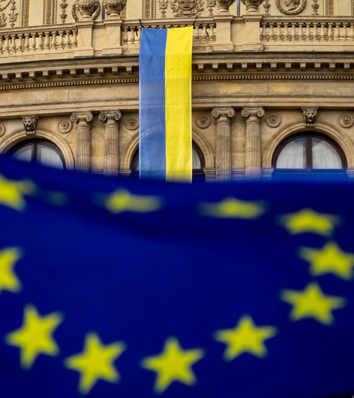 Flagge der EU im Vordergrund, im Hintergrund die Flagge der Ukraine an einer Gebäudefassade