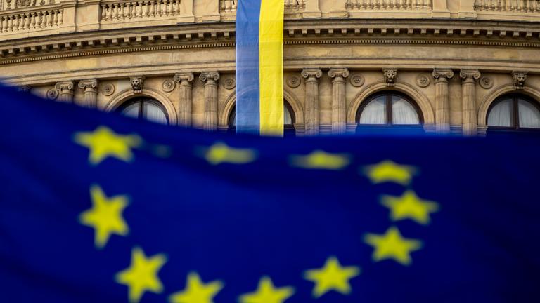 Flagge der EU im Vordergrund, im Hintergrund die Flagge der Ukraine an einer Gebäudefassade