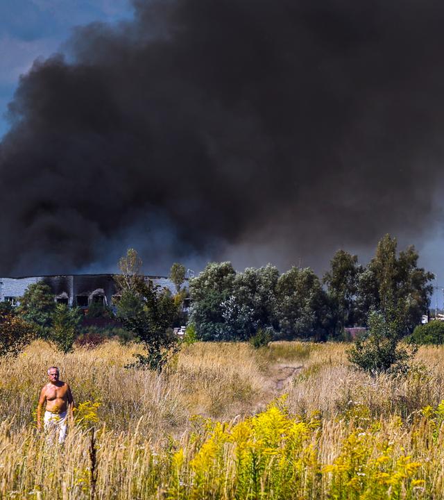 Menschen gehen über ein Feld, während an der Einschlagstelle eines russischen Angriffs nahe Kiew (Ukraine) am 31. August 2026 Rauch aufsteigt – inmitten der russischen Invasion.