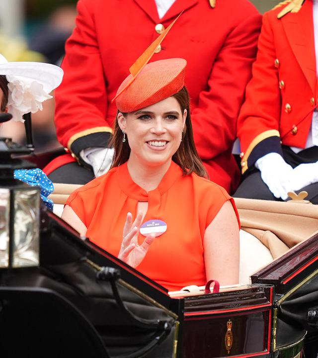 Auf dem Bild ist Prinzessin Eugenie zu sehen. Diese sitzt in einer offenen schwarze Kutsche. Sie trägt ein leuchtenden orangefarbenes Kleid mit passendem Hut.