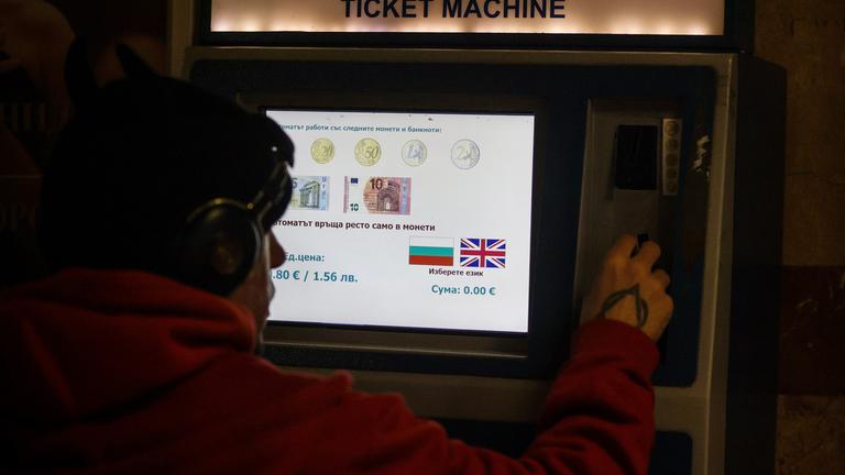 Eine Person kauft Fahrkarten an einem Automaten, auf dem angegeben ist, welche Euro-Banknoten und -Münzen akzeptiert werden, da das Land der Euro-Währungsunion beitritt.