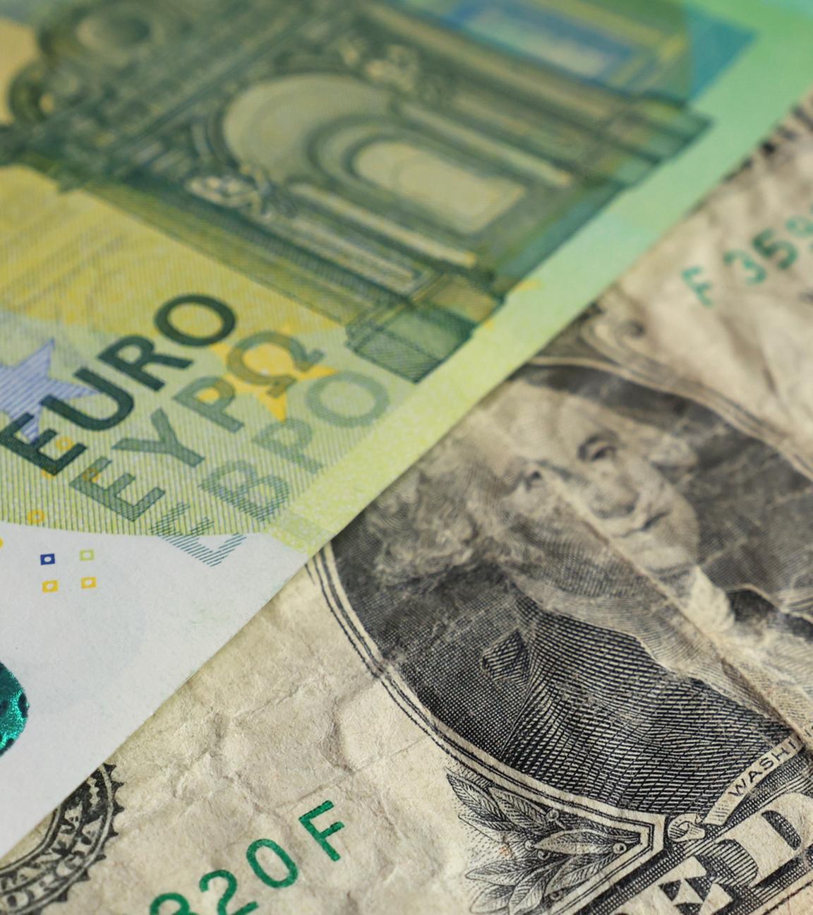 Ein US-Dollar liegt unter einer 100 Euro Banknote. 