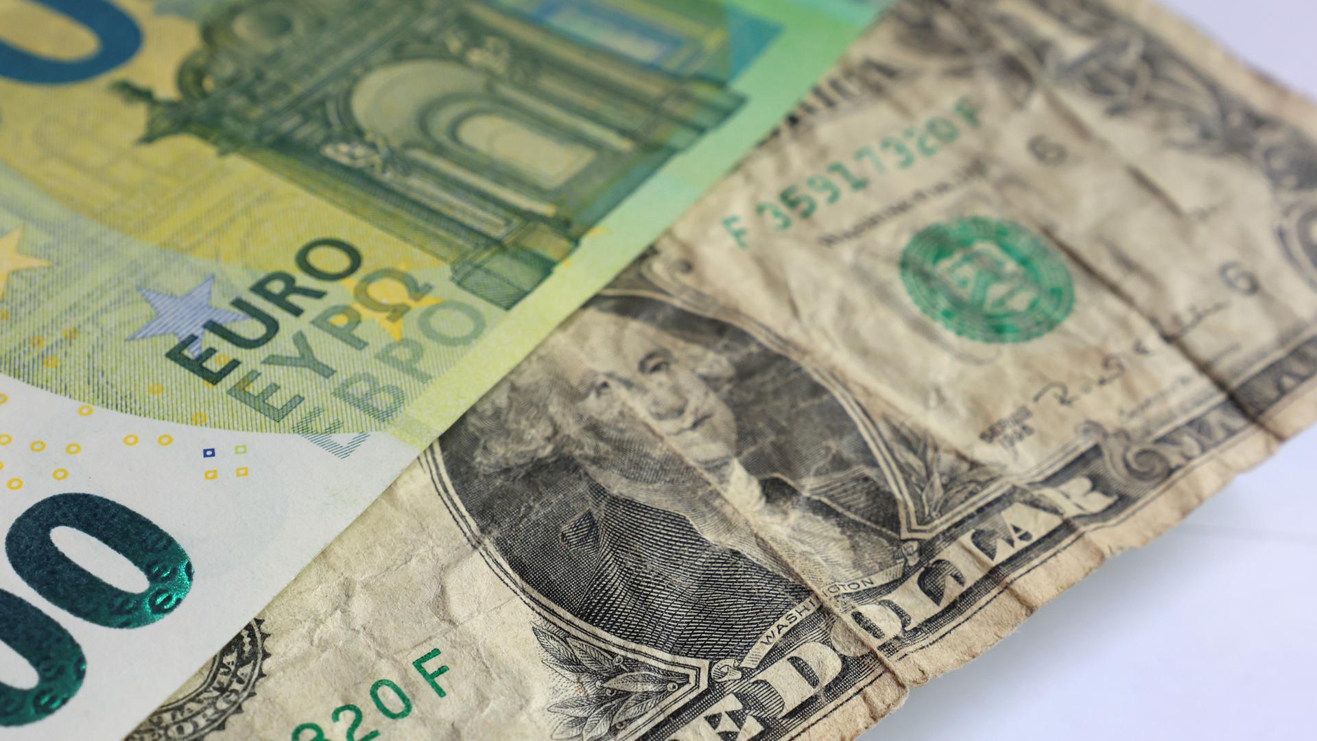 Ein US-Dollar liegt unter einer 100 Euro Banknote. 