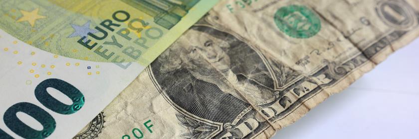 Ein US-Dollar liegt unter einer 100 Euro Banknote. 