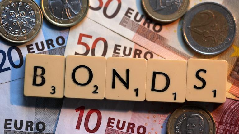 Der Schriftzug Bonds liegt auf Euro-Geldscheinen neben Euro-Münzen.