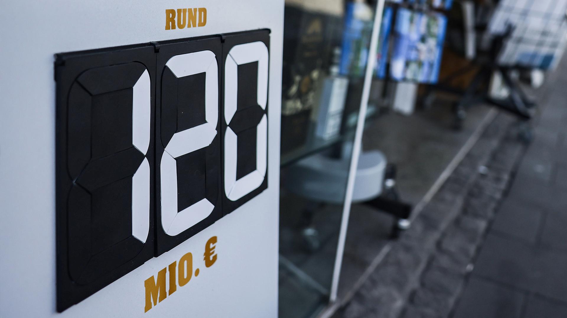 Ein Schild mit der Aufschrift "rund 120 Millionen Euro" steht vor einem Tabak- und Zeitschriften-Geschäft in Düsseldorf