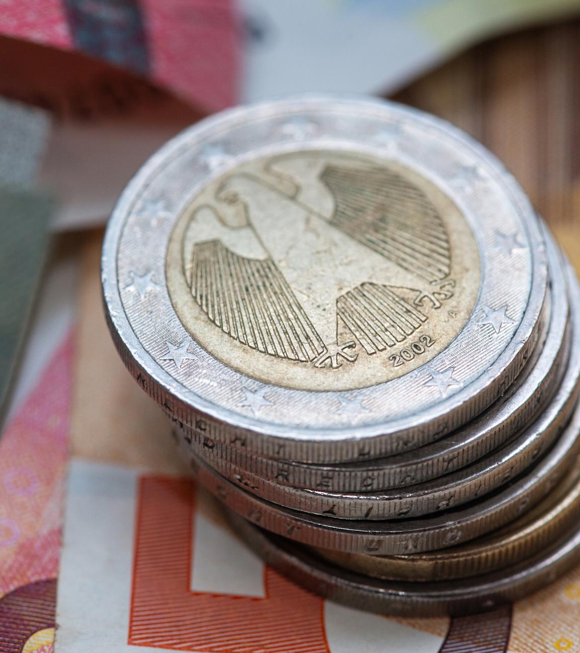 Symbolbild:  Ein Stapel Zwei-Euro-Münzen liegt auf verschiedenen Euro-Banknoten.