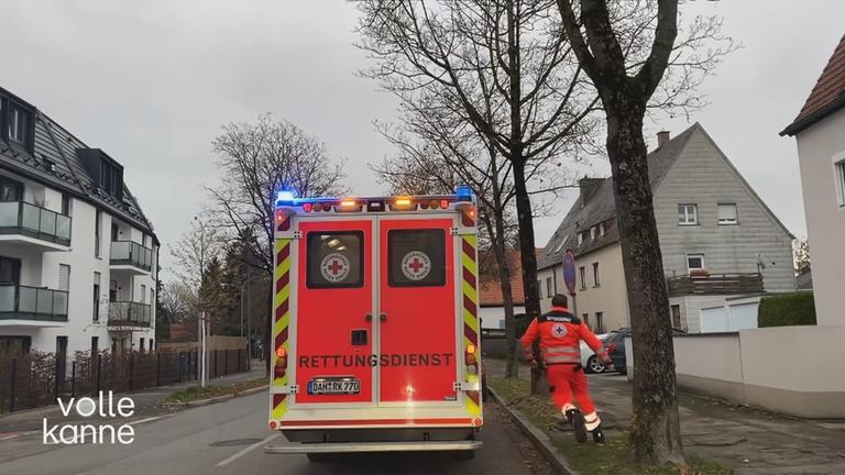 Eine Rettungskraft rennt zu einem Rettungswagen. Das Blaulicht ist an.