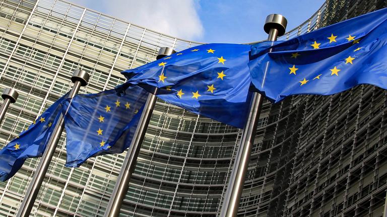 Blaue Europafahnen wehen vor einem modernen großen Gebäude.