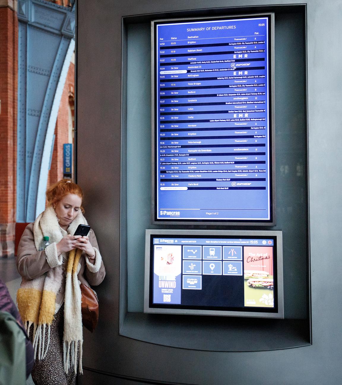 Bahnreisende stehen vor einer Anzeigetafel am Bahnhof und überprüfen Verbindungen