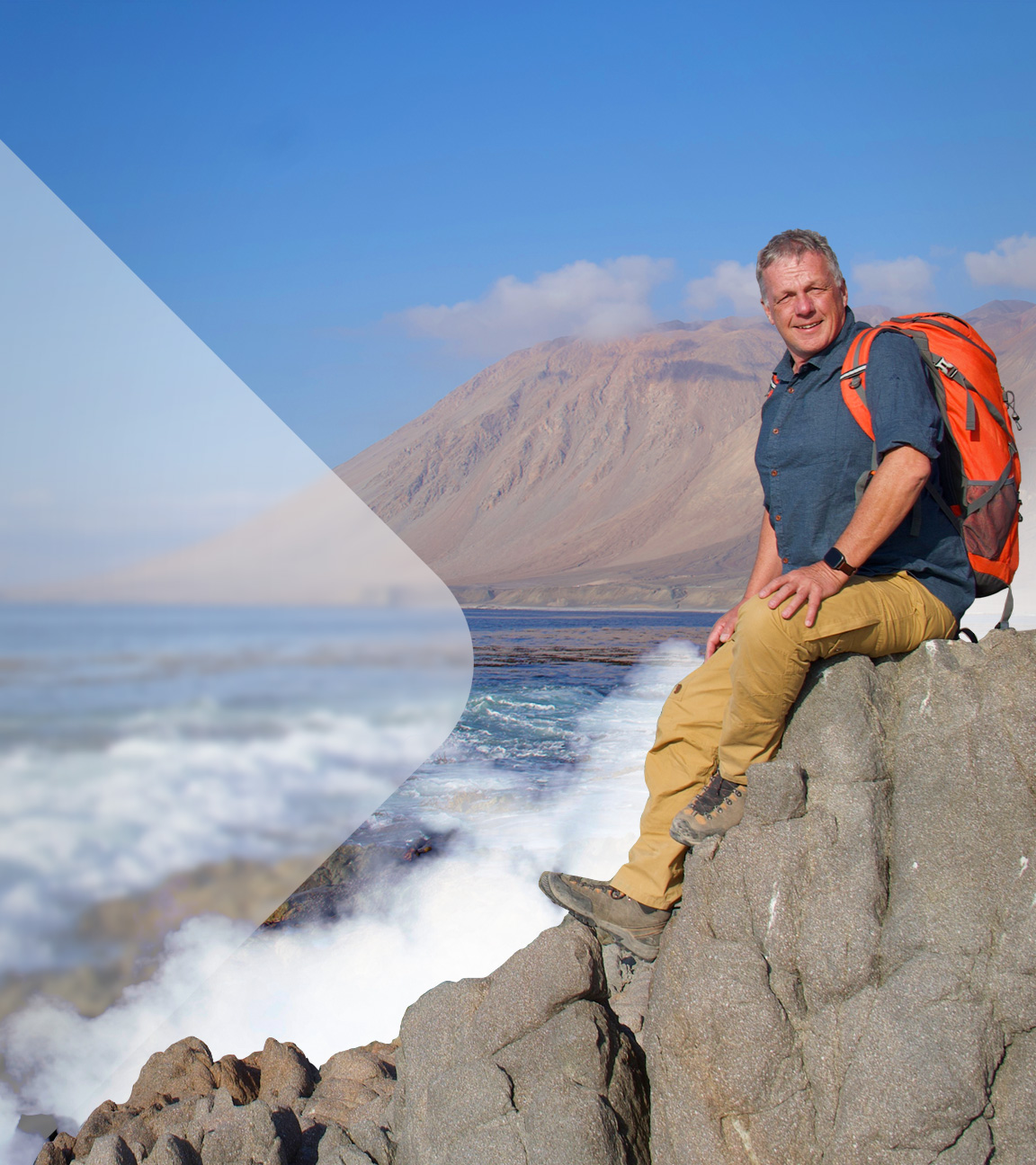 Geologe Colin Devey sitzt rechts mit Rucksack auf einem Felsen, links ein felsiger Küstenstreifen und eine Bergkette vor blauem Himel im Hintergrund.