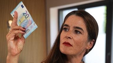 Eine Frau sitzt an einem Tisch und hält einen 20-Euro-Schein in der Hand.