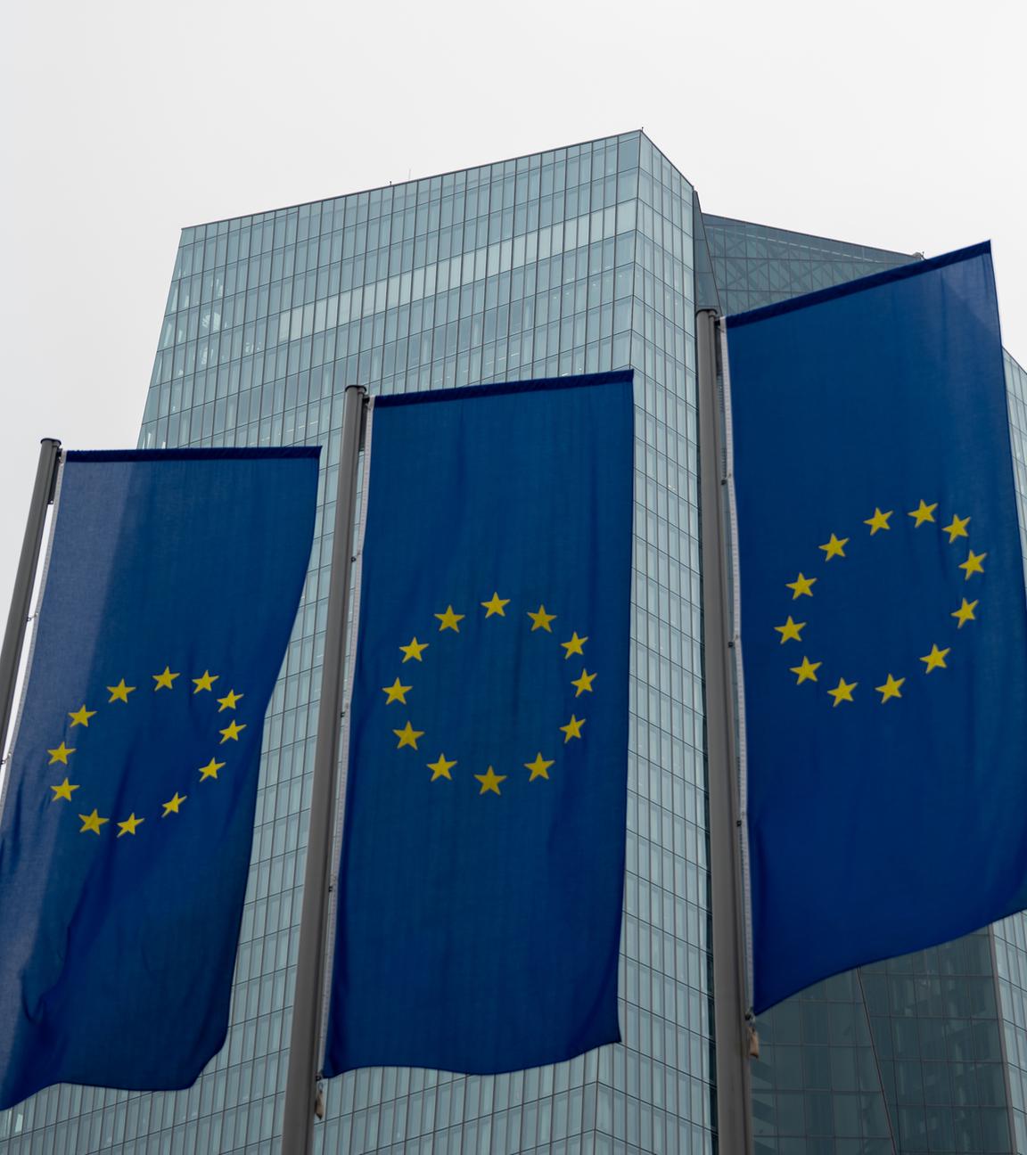 Vier EU-Flaggen aus Froschperspektive vor dem Hochhaus der Europäischen Zentralbank in Frankfurt