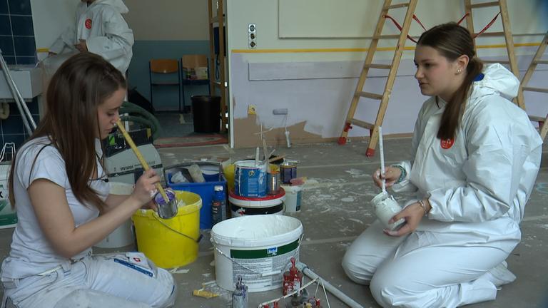 Zwei Schülerinnen helfen beim Streichen der Wand.