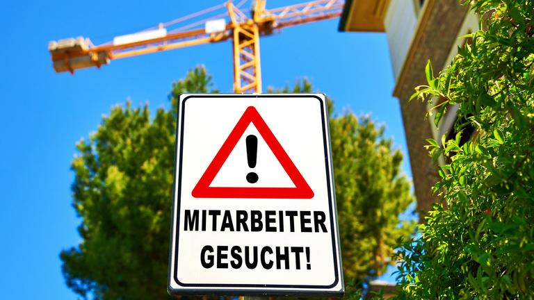 Ein Warnschild mit der Aufschrift: Mitarbeiter gesucht! an einer Baustelle