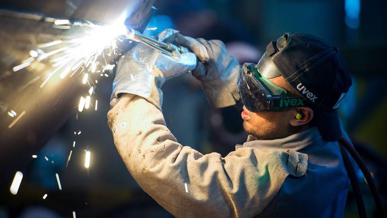 Eine zuvor als Schweißer ausgebildete Person arbeitet an einem Stahlsegement für einen Windradturm. Fürstenwalde, Brandenburg.