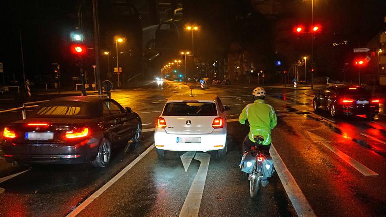 Fahrradfahrer mit Warnweste und Reflektoren wartet im Dunkeln an einer Ampel im Straßenverkehr.