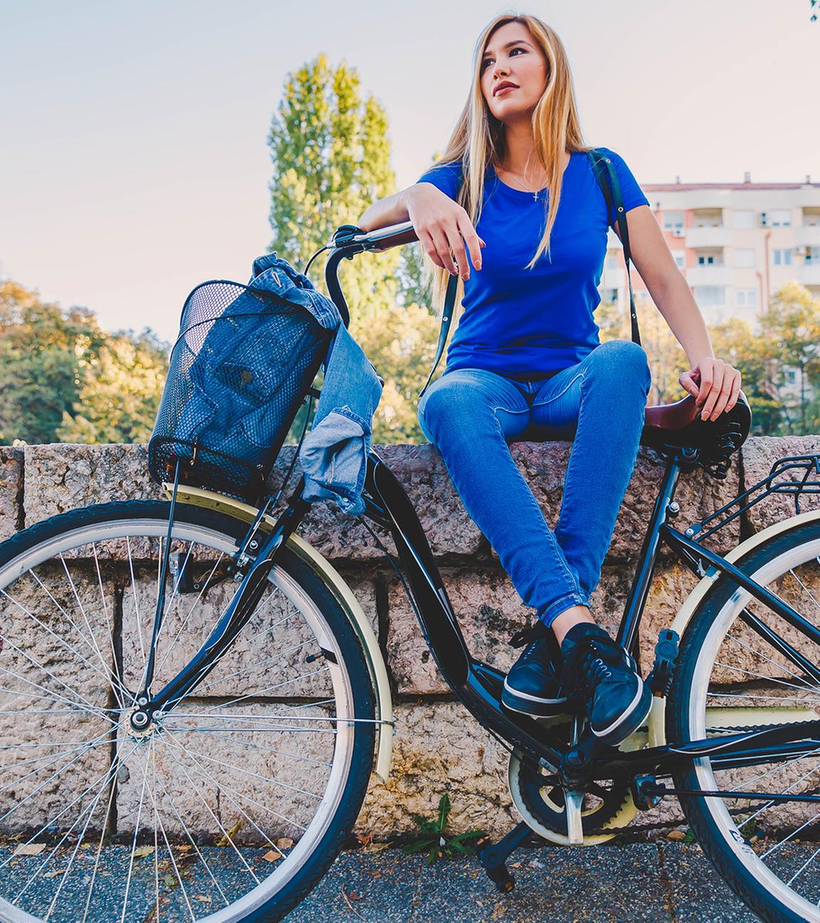 Frau sitzt auf einer Mauer, davor angelehnt steht ihr Fahrrad