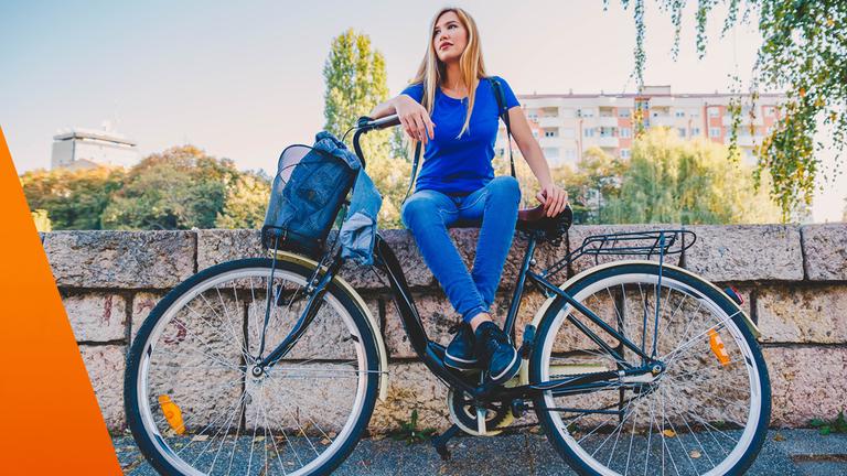 Frau sitzt auf einer Mauer, davor angelehnt steht ihr Fahrrad